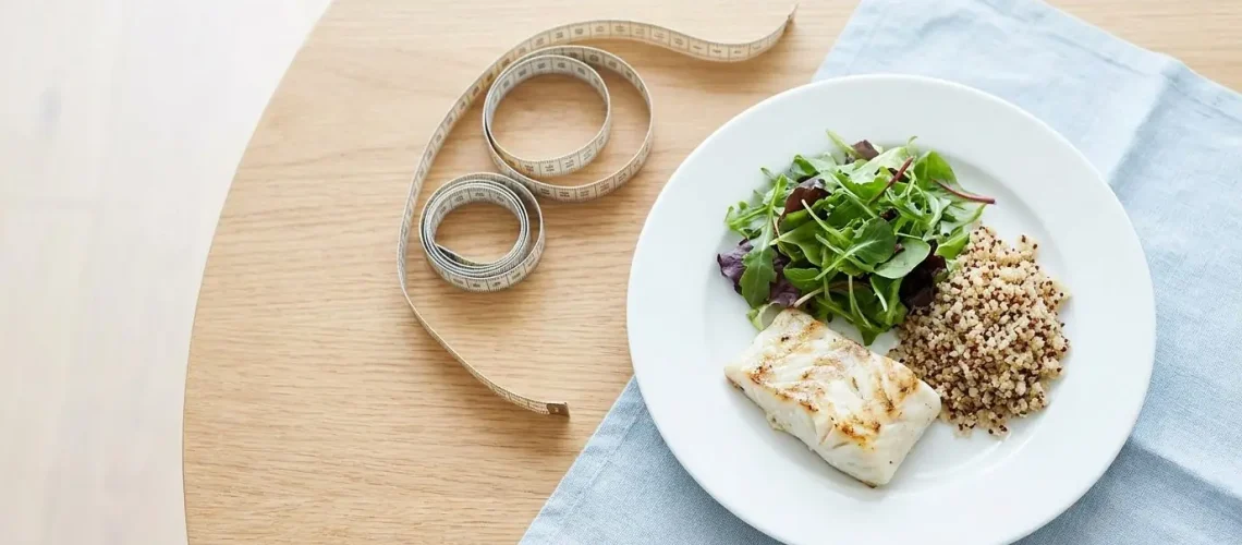Portion-controlled healthy meal with grilled fish, salad and quinoa beside a measuring tape